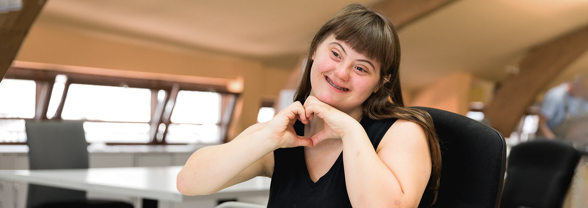 Eine junge Frau mit Downsyndrom bildet mit ihren Händen ein Herz.